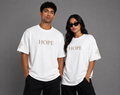 Male and female models wearing white Hope T-shirts with embroidered HOPE chest lettering and embroidered cross sleeve details from the Soul Kreations Luxe Promise Collection.