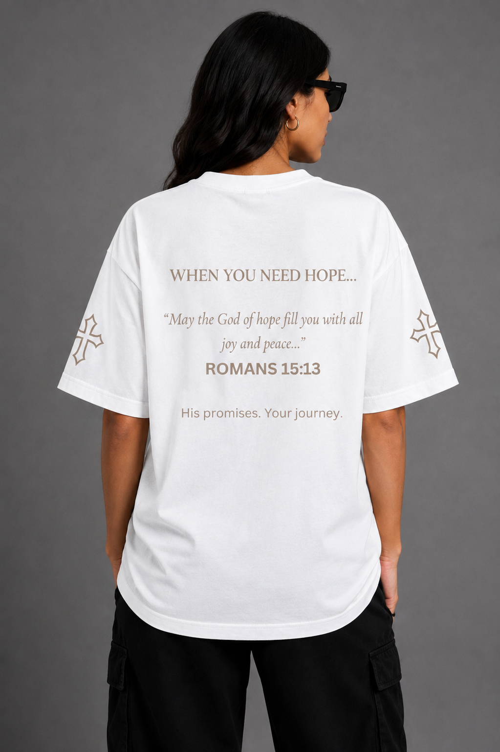 Female model wearing white Hope T-shirt from the Promise Collection, featuring Romans 15:13 scripture printed on the back and embroidered cross details on the sleeves.