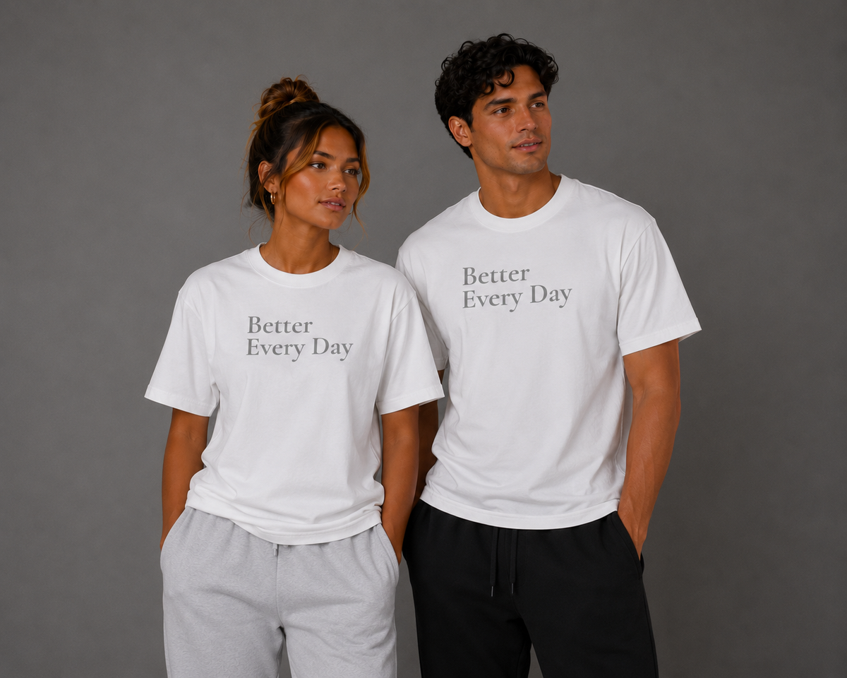 Woman and man wearing matching white “Better Every Day” motivational T-shirts, standing together against a gray studio background.