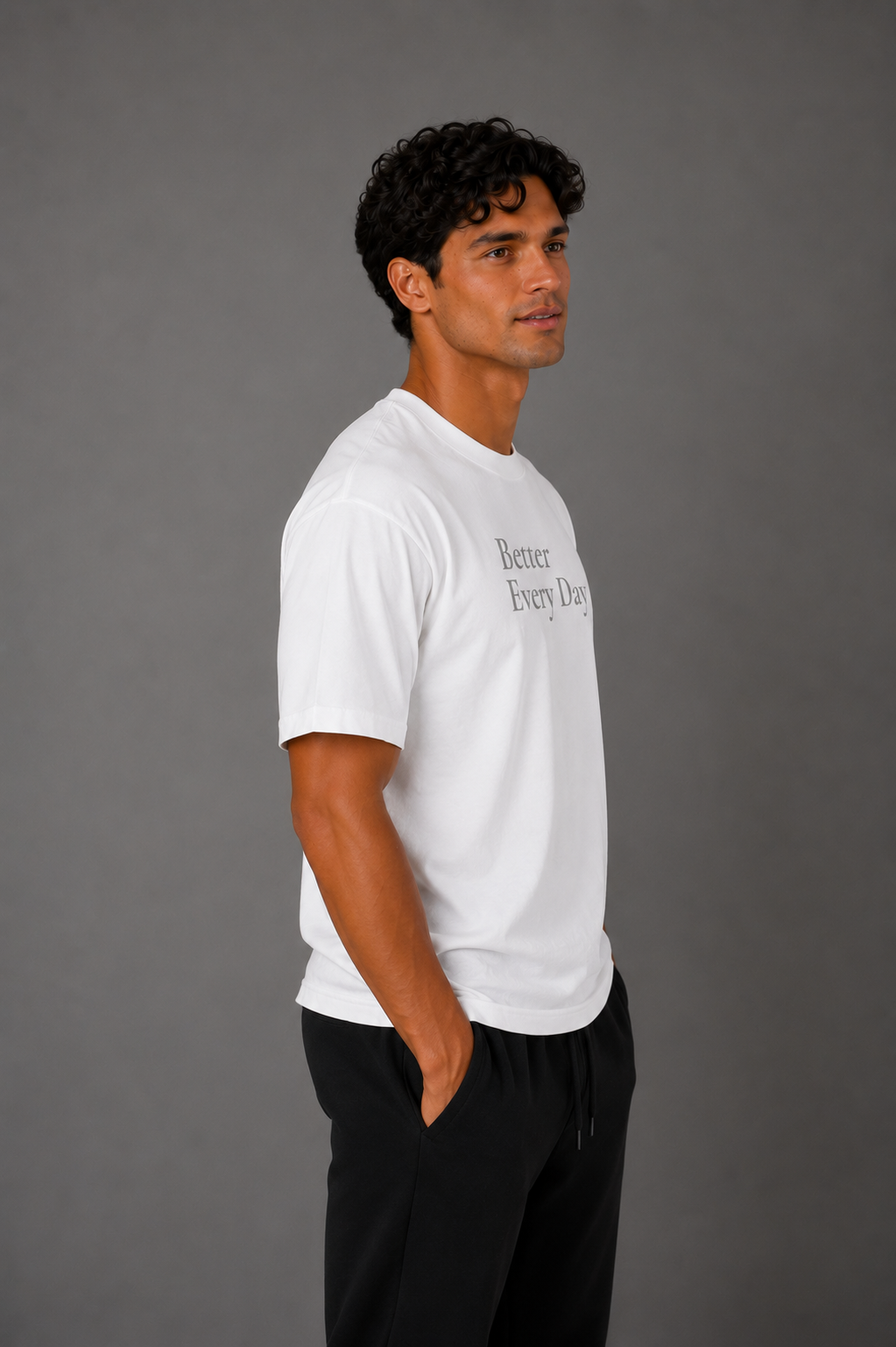 Man wearing a white “Better Every Day” motivational T-shirt shown from the side against a gray studio background.