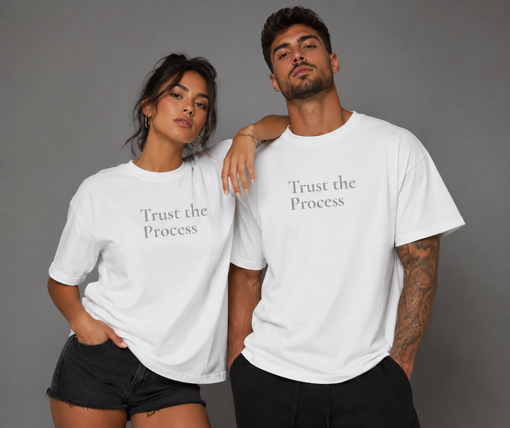 Man and woman modeling matching white “Trust the Process” motivational T-shirts against a gray studio background.