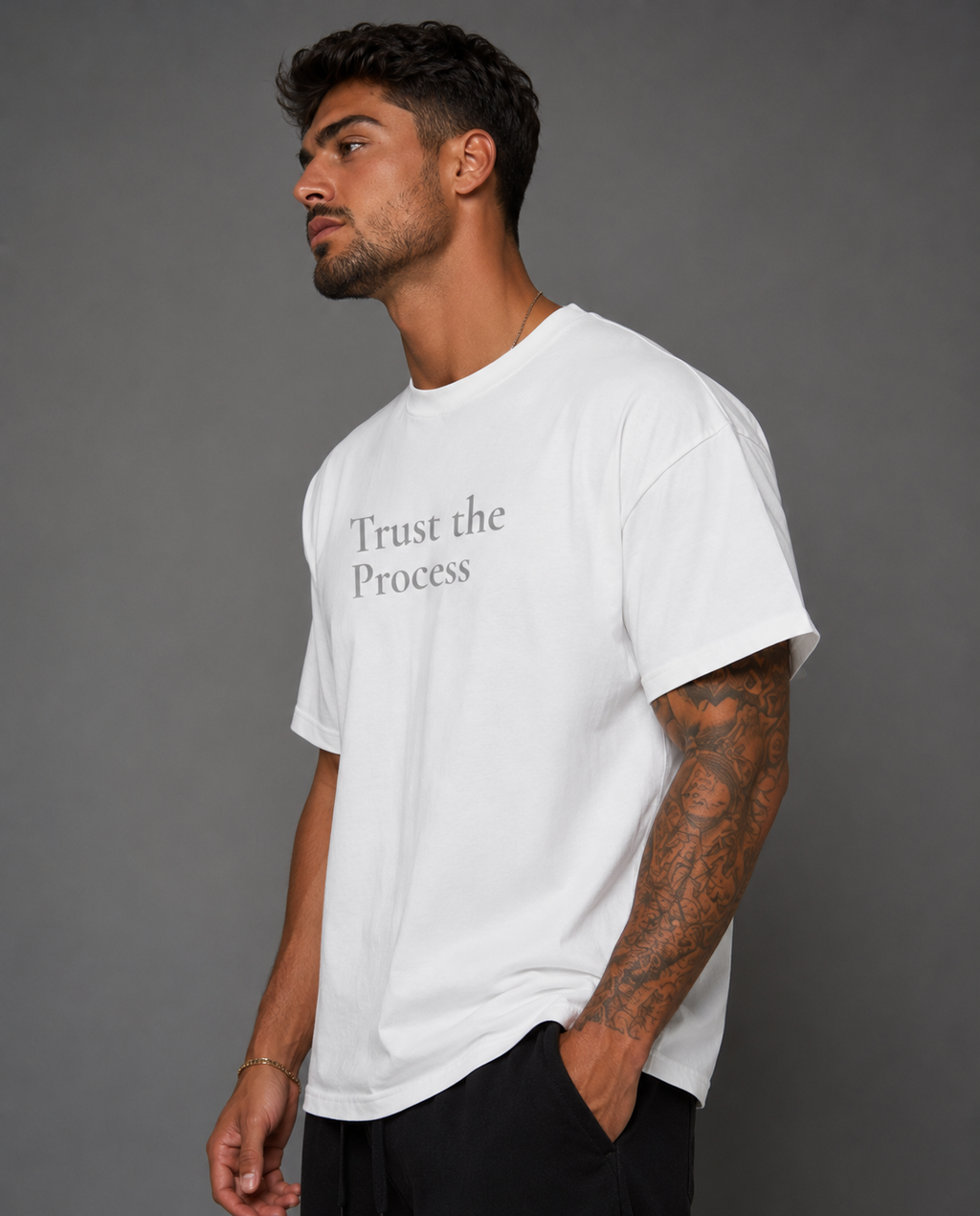 Man modeling a white “Trust the Process” motivational T-shirt from the side against a gray studio background.