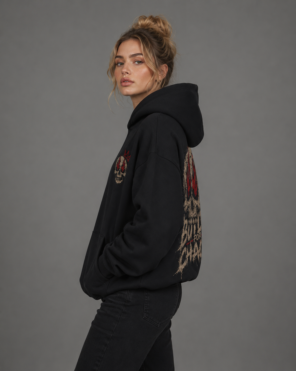 Side view of a female model wearing a black “Built for Chaos” hoodie featuring a small skull chest graphic and large distressed skull-and-flame back design.