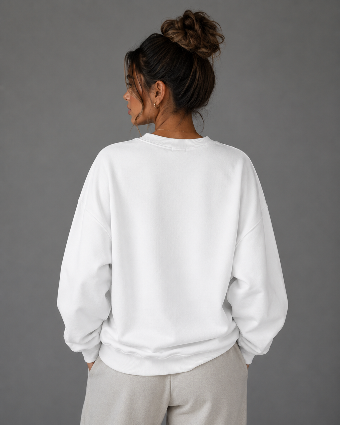 Back view of a female model wearing a white oversized “Wear Your Energy” sweatshirt, styled with neutral sweatpants.