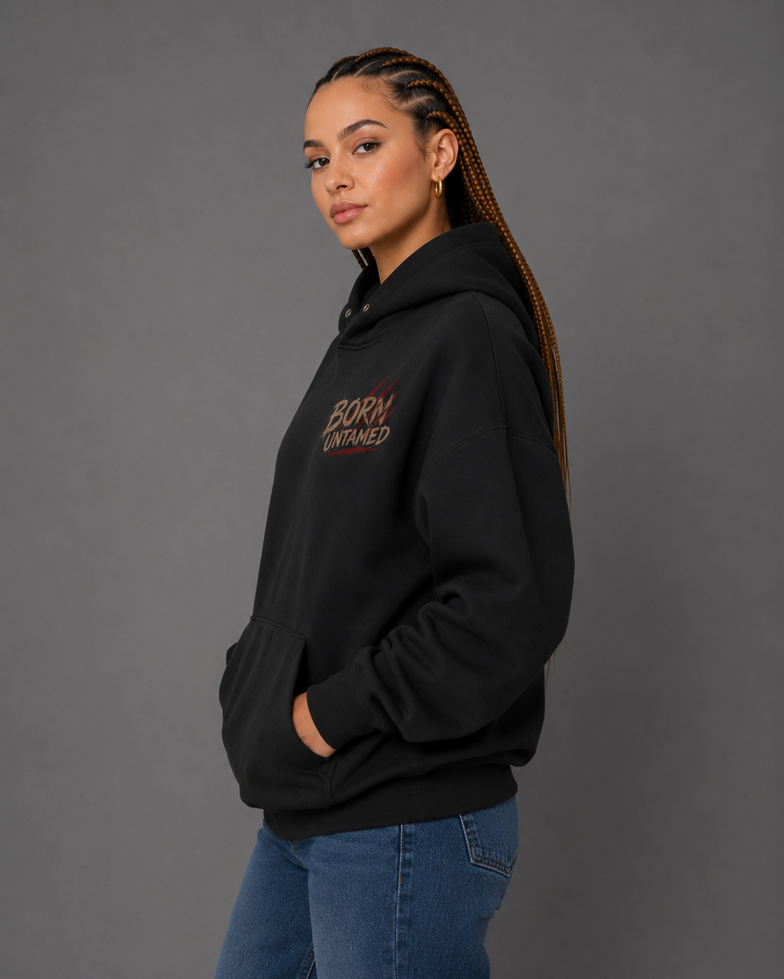 Female model wearing a black “Born Untamed” hoodie in a side view, showcasing the small distressed chest graphic with red accents.