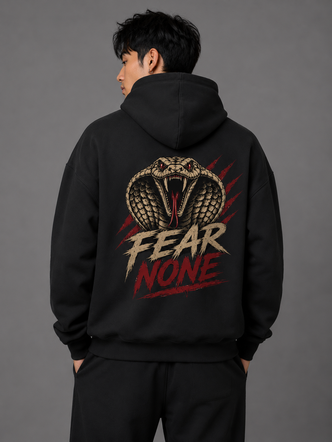Male model showcasing the back of a black “Fear None” hoodie featuring a large striking cobra graphic, red claw marks, and bold distressed “Fear None” lettering.