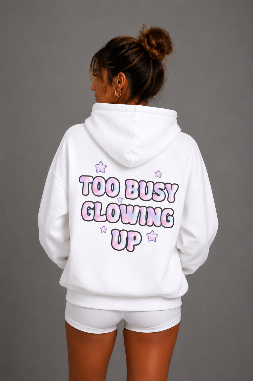 Woman modeling white Too Busy Glowing Up hoodie with pink star graphics on back