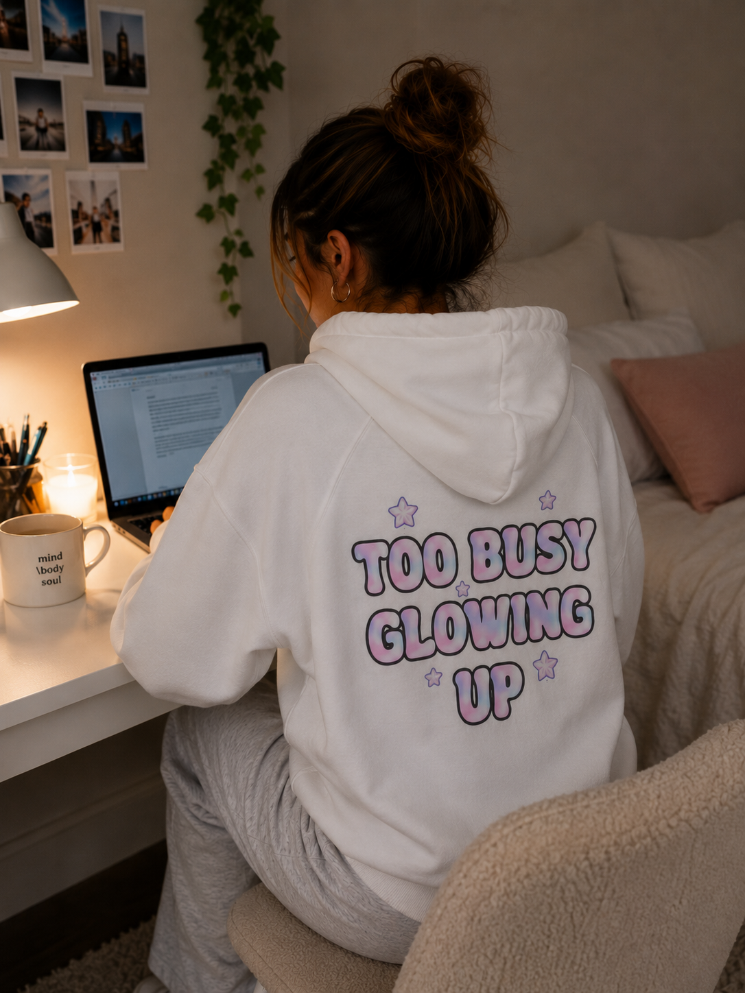 Woman wearing white Too Busy Glowing Up hoodie while working at a desk