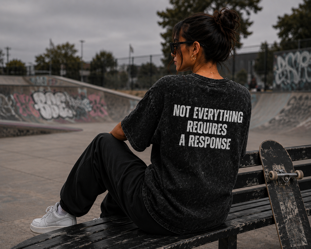Woman wearing black washed oversized graphic T-shirt with “Not Everything Requires a Response” back design at a skatepark