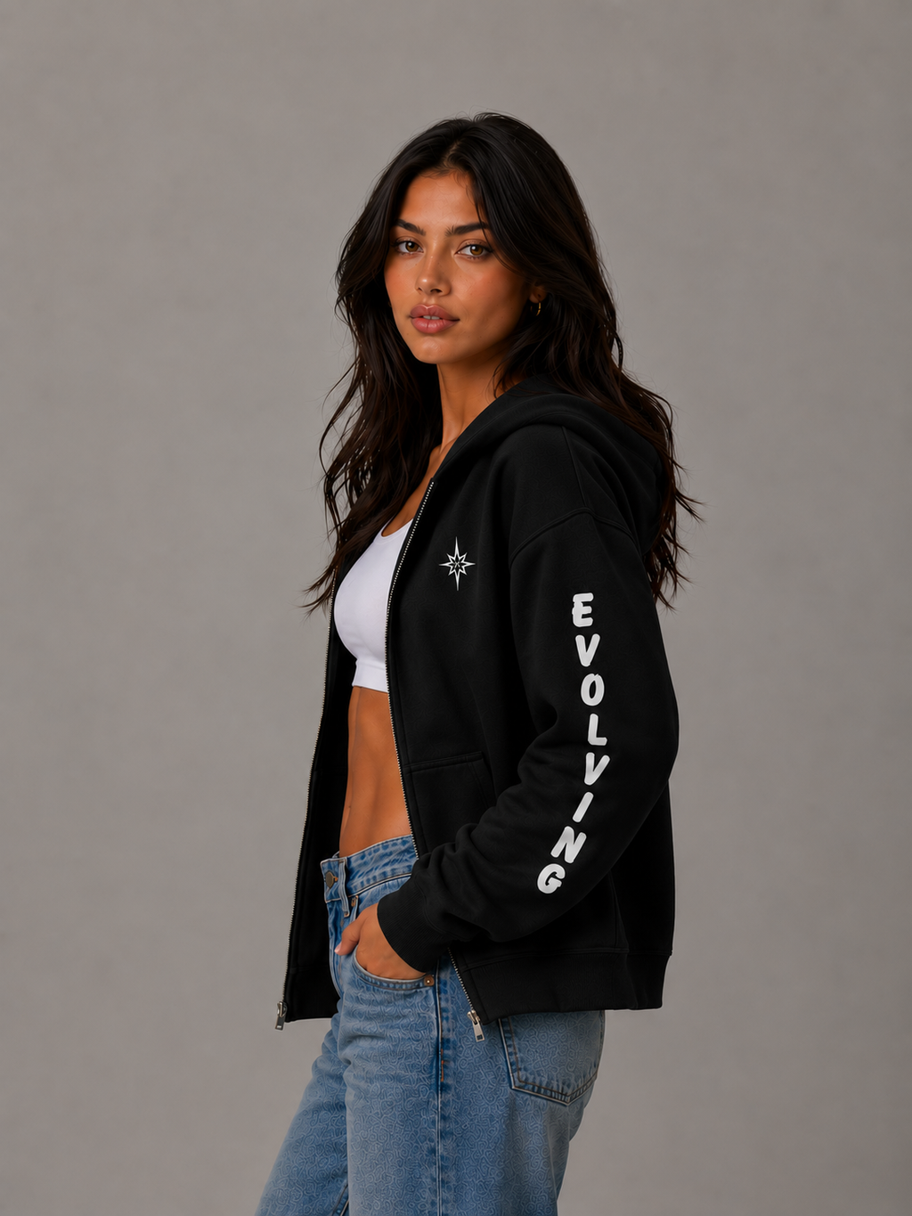 Female model wearing a black Gently Evolving full-zip hoodie, shown from the side with white “EVOLVING” sleeve lettering and embroidered star detail.