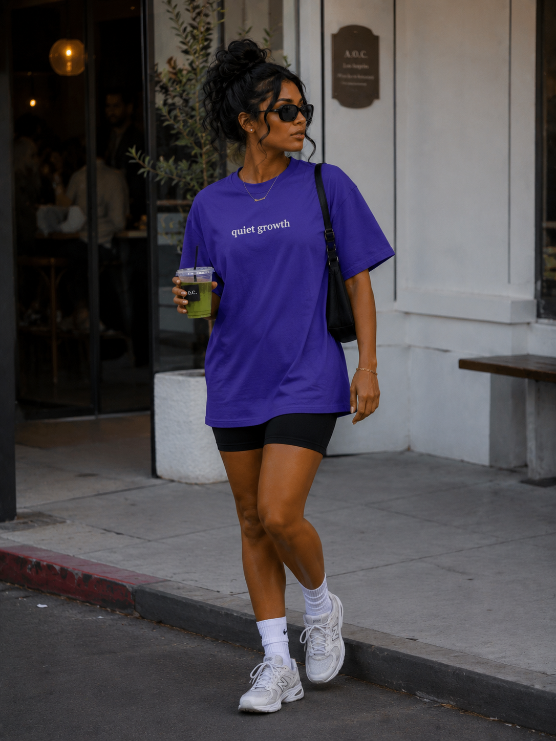 Woman wearing purple Quiet Growth oversized T-shirt while walking outside a café