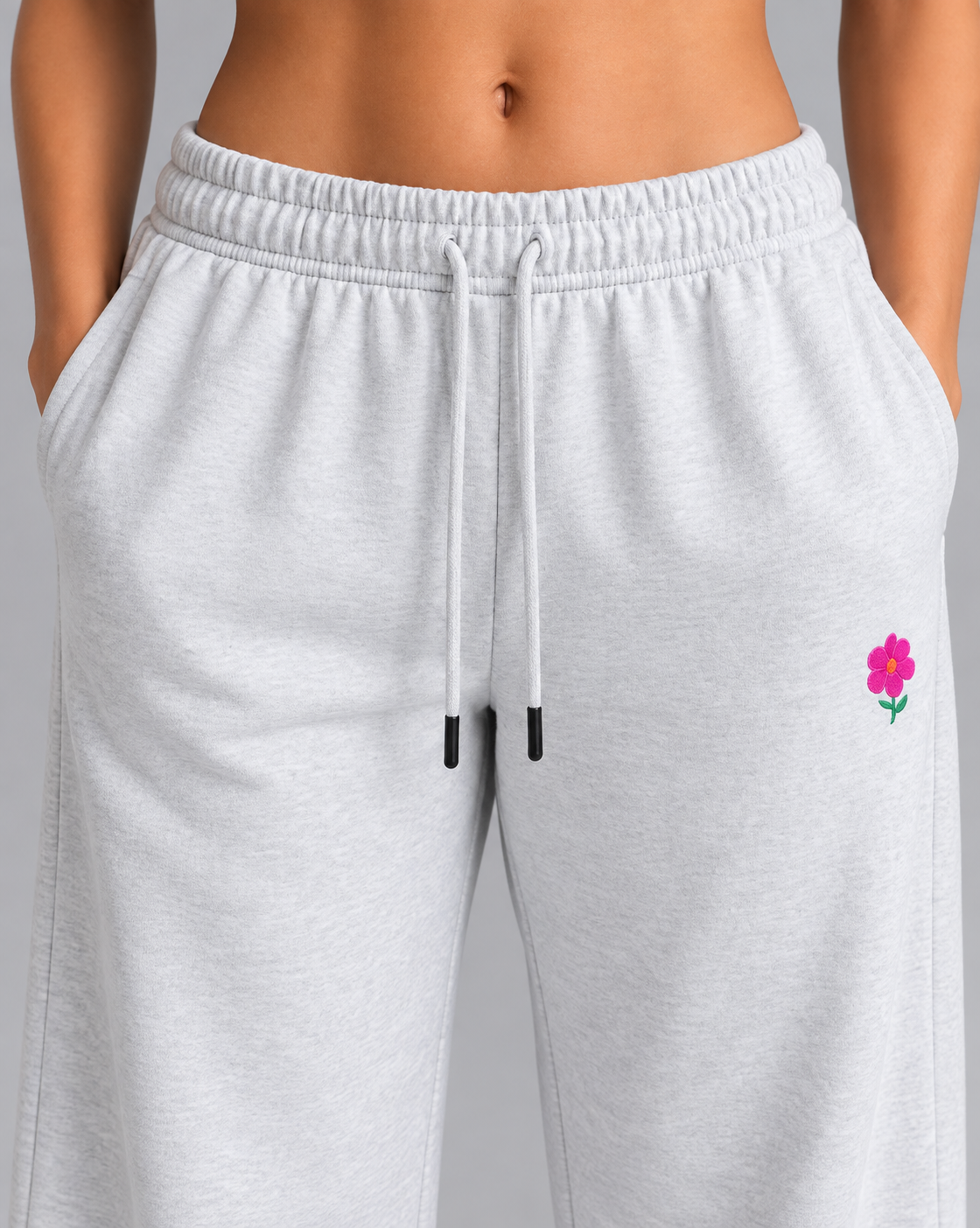 Close-up of light heather gray sweatpants with small pink flower embroidery on the thigh