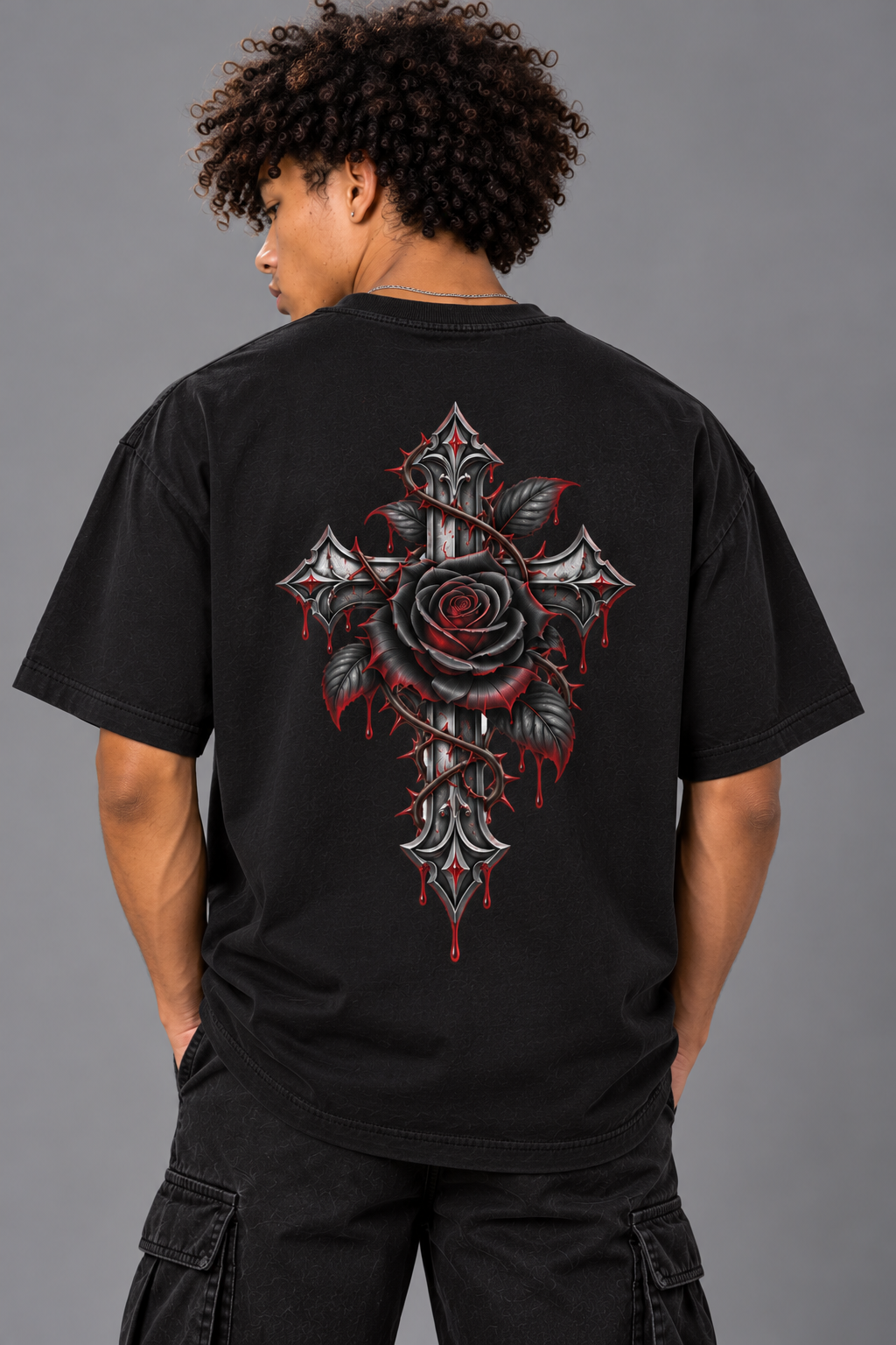 A person shown from the back wearing a black short-sleeve T-shirt with a large graphic print on the back featuring a cross and rose design in red, gray, and black, paired with black cargo pants against a plain gray studio background.