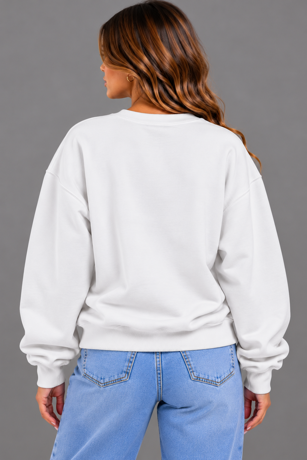 A woman shown from the back wearing a plain white crewneck sweatshirt and light blue jeans against a solid gray studio background.