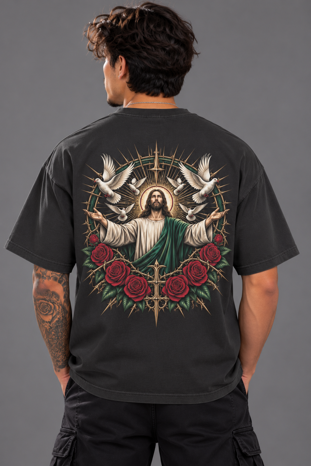 A man viewed from behind wearing a black t-shirt with a large graphic print of Jesus Christ surrounded by doves, roses, and a cross on the back, set against a solid gray background.